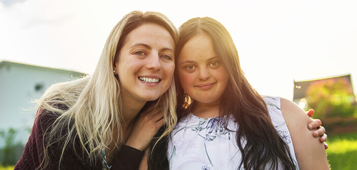Aile dostu ile gün batımında dışarıda gülümseyen Trisomie 21 yetişkin kızın portresi