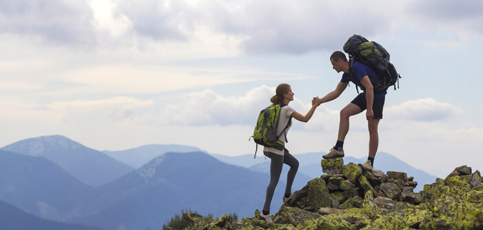 deux personnes faisant de la randonnée dans les montagnes - l'homme aide la femme à monter sur un tas de pierres